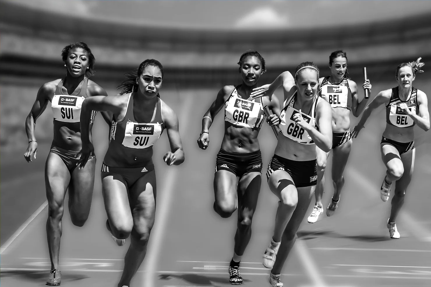 Black and white photo of female relay runners racing on a track in national team kits