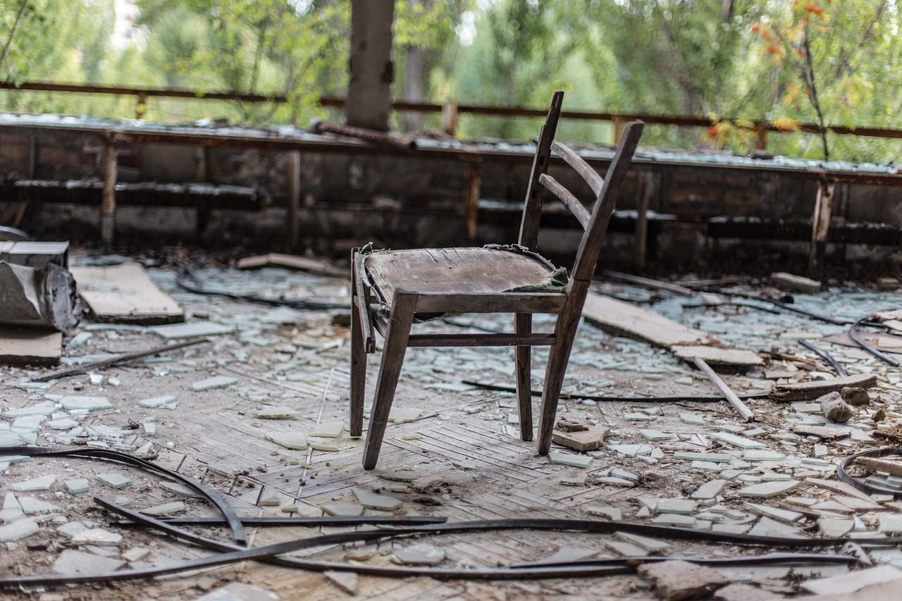 Lone wooden chair standing amid broken glass and debris in an abandoned war-damaged room